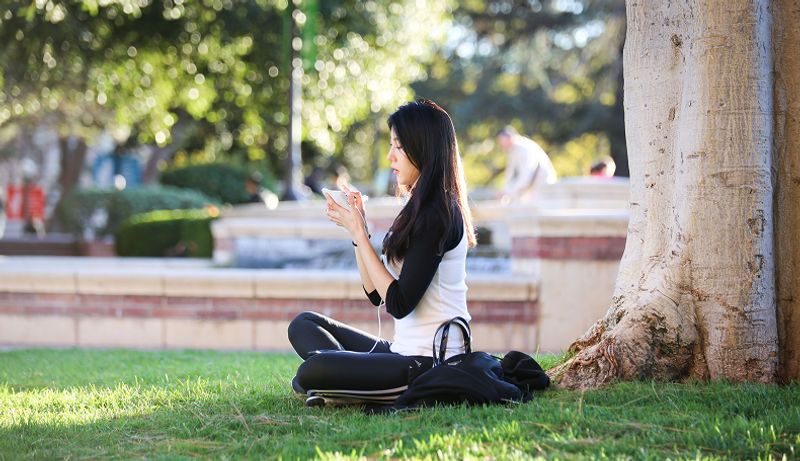 A girl listens to music while sitting on the grass in Dickson Court North