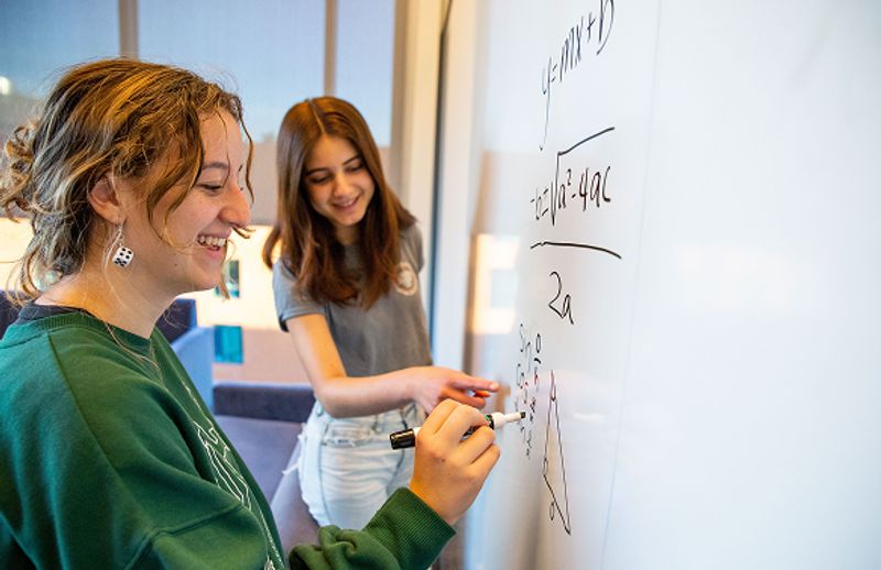 Two students doing math on a whiteboard.