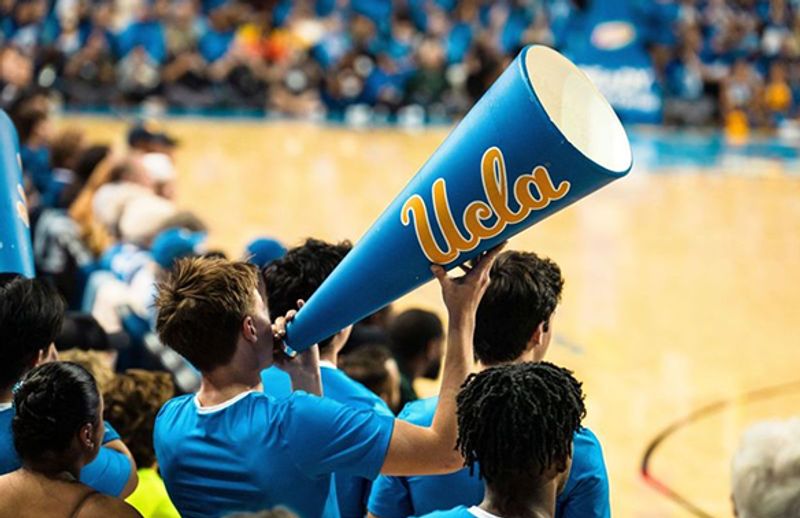 Student holding a blue UCLA metaphone at an indoor sports game.