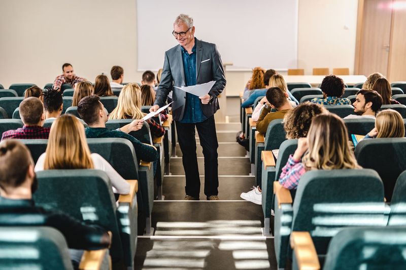 An instructor distributes papers to students seated in a large university lecture hall during class
