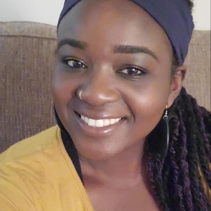 Headshot of Black woman wearing a blue headband, braids, and a yellow shirt