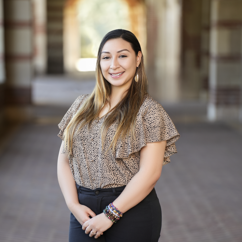 Headshot of woman with brunette hair wearing a beige blouse and black trousers