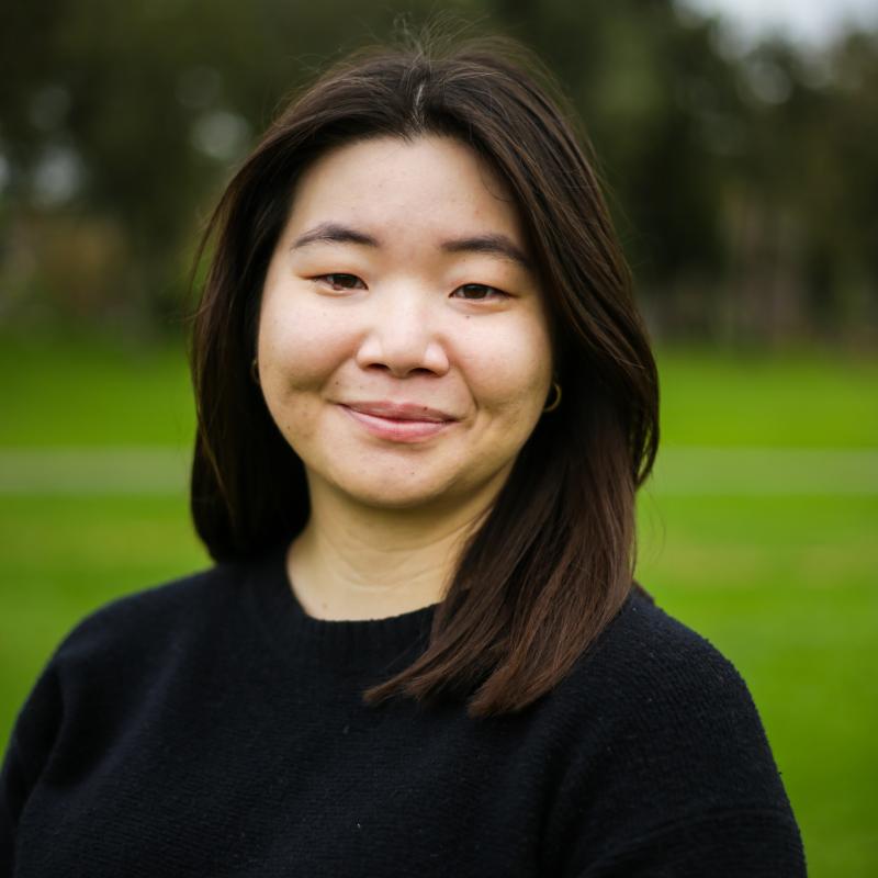 Headshot of Asian American women wearing a black blouse and standing in front of a green field